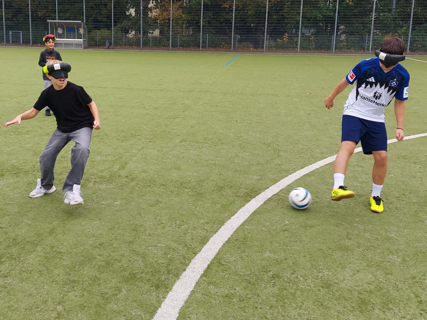 Zwei Schüler probieren Blindenfussball auf dem Rasen aus