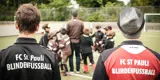 Hinter den Rücke zweier Guides in FC St. Pauli Blindenfussball-Jacken tummeln sich die Kinder um Serdal, um den Ball zu erwischen
