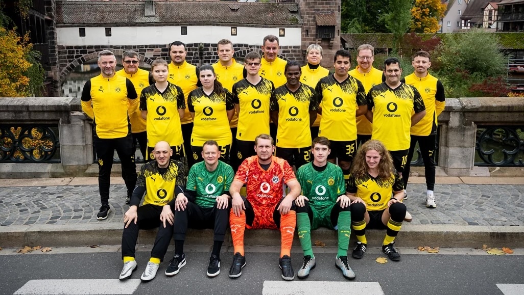 Das Team gruppiert sich in drei Reihen auf einer Straße vor einer Altstadt